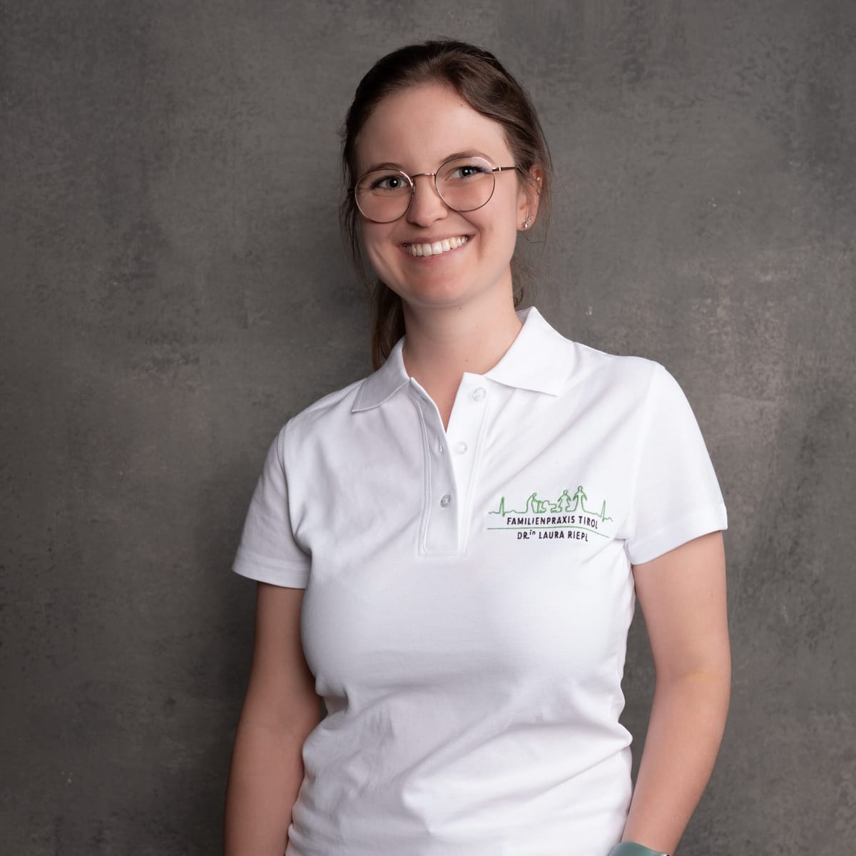 Dr.in Laura Riepl in weißer Praxisbekleidung vor grauem Hintergrund.